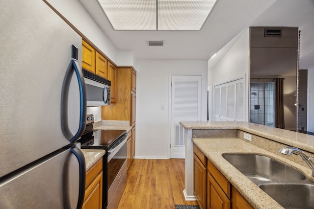 kitchen featuring light stone countertops, appliances with stainless steel finishes, sink, and light wood-type flooring