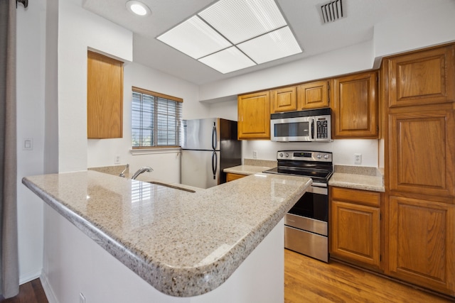 kitchen featuring appliances with stainless steel finishes, kitchen peninsula, sink, and light stone countertops