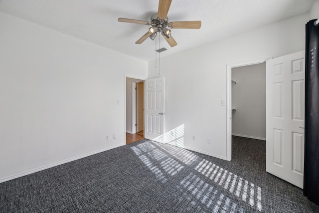 unfurnished bedroom with ceiling fan, a walk in closet, and dark carpet