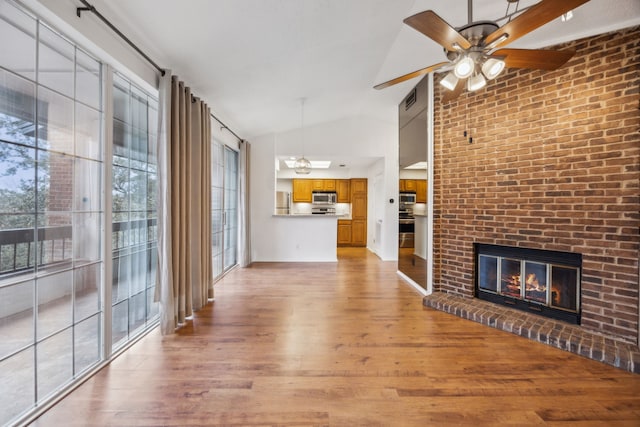 unfurnished living room with ceiling fan, high vaulted ceiling, a brick fireplace, and light hardwood / wood-style flooring