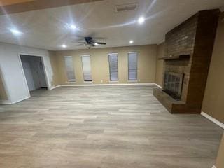 unfurnished living room with ceiling fan, light wood-type flooring, and a brick fireplace