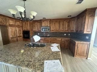 kitchen featuring decorative light fixtures, an inviting chandelier, sink, tasteful backsplash, and stone counters