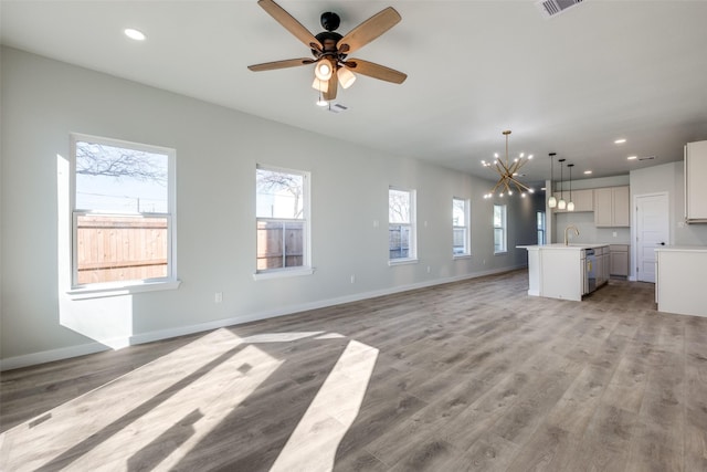 unfurnished living room with ceiling fan with notable chandelier and light hardwood / wood-style flooring