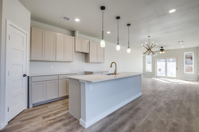 kitchen with sink, an island with sink, pendant lighting, ceiling fan with notable chandelier, and light wood-type flooring