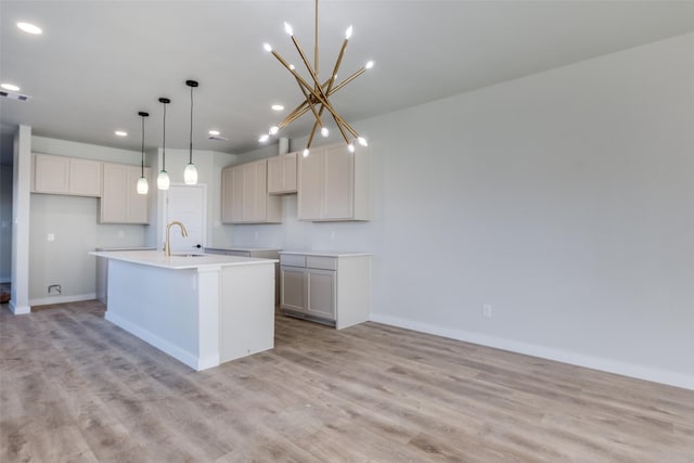 kitchen with sink, hanging light fixtures, an island with sink, light hardwood / wood-style floors, and a chandelier