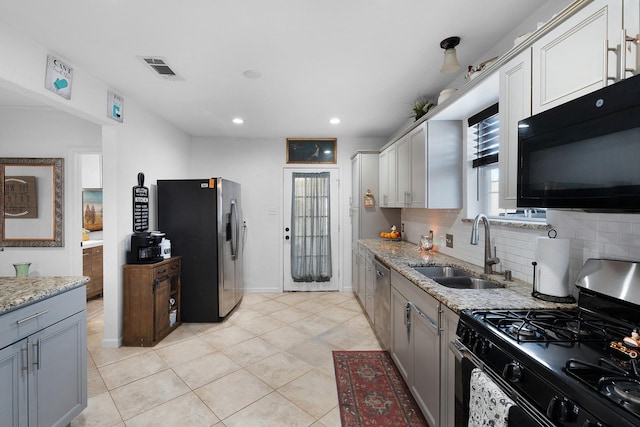 kitchen featuring sink, decorative backsplash, gray cabinets, appliances with stainless steel finishes, and light stone counters