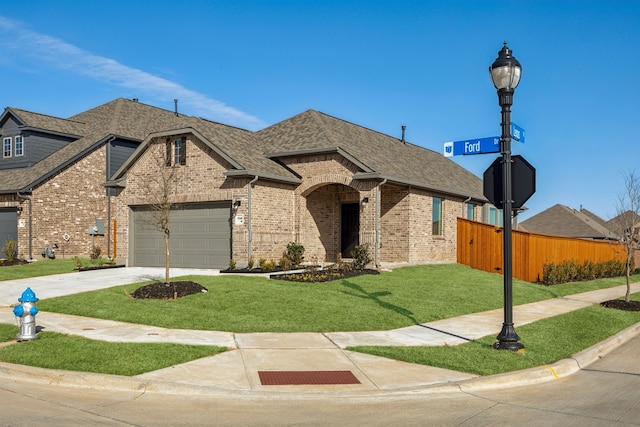 french country home with a front yard, fence, a shingled roof, a garage, and brick siding