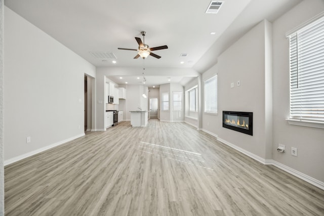 unfurnished living room with ceiling fan, baseboards, visible vents, and light wood-type flooring