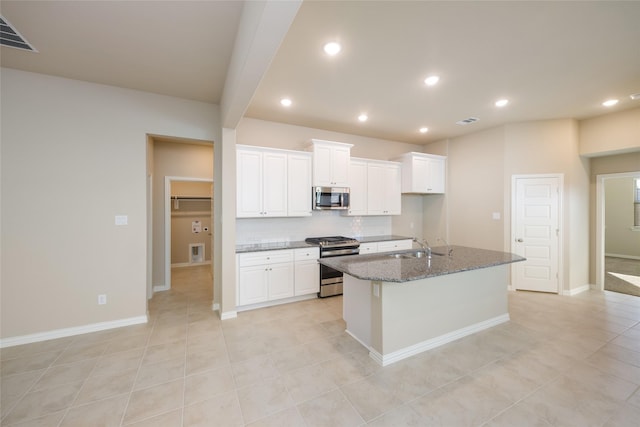 kitchen with appliances with stainless steel finishes, tasteful backsplash, white cabinets, a center island with sink, and dark stone counters