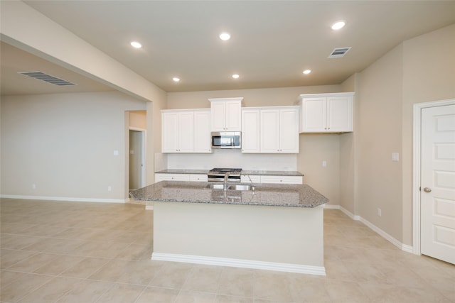 kitchen featuring sink, white cabinets, light tile patterned floors, light stone counters, and a center island with sink