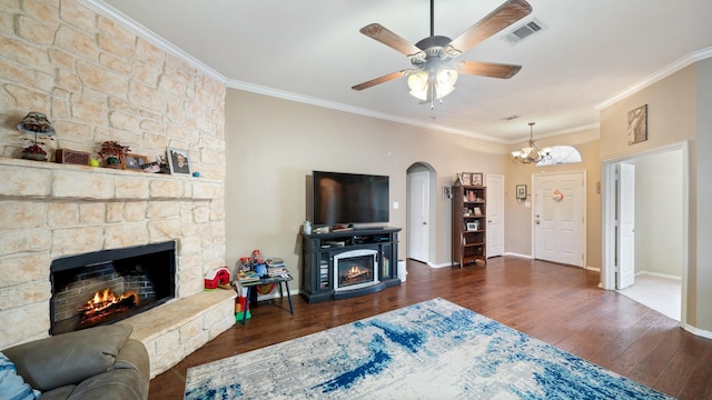 living room with dark hardwood / wood-style flooring, a stone fireplace, crown molding, and ceiling fan with notable chandelier