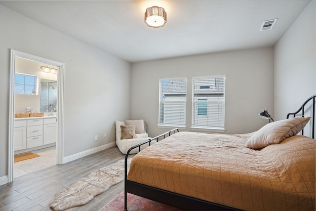 bedroom featuring multiple windows, connected bathroom, and light hardwood / wood-style flooring