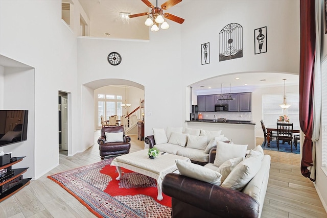 living area featuring stairs, light wood-style floors, arched walkways, and ceiling fan