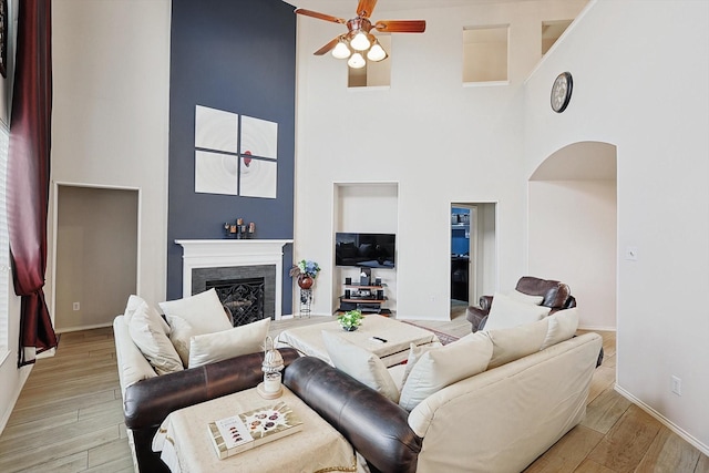 living area with light wood finished floors, a fireplace, baseboards, and ceiling fan