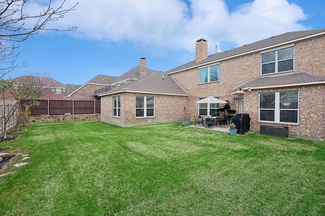 back of house featuring a lawn, a patio, a fenced backyard, brick siding, and a chimney