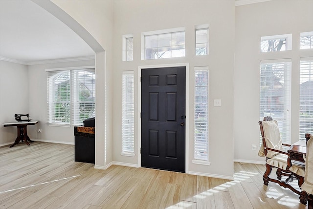 foyer entrance with light wood-style flooring, baseboards, arched walkways, and ornamental molding