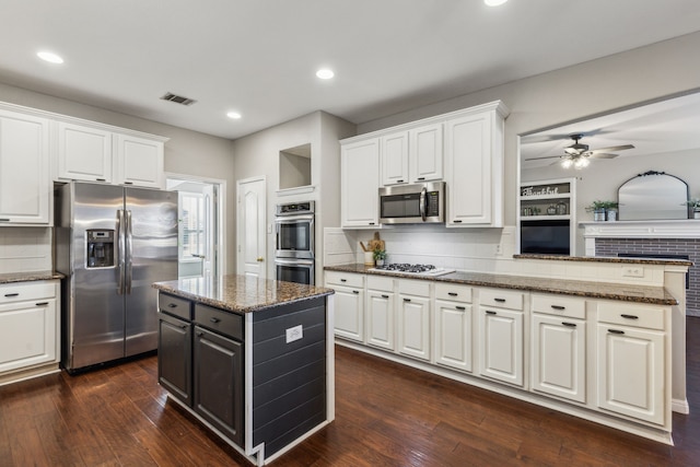 kitchen with appliances with stainless steel finishes, white cabinetry, dark hardwood / wood-style flooring, decorative backsplash, and ceiling fan