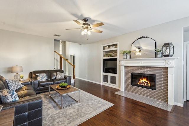 living room featuring ceiling fan, built in shelves, dark hardwood / wood-style floors, and a fireplace