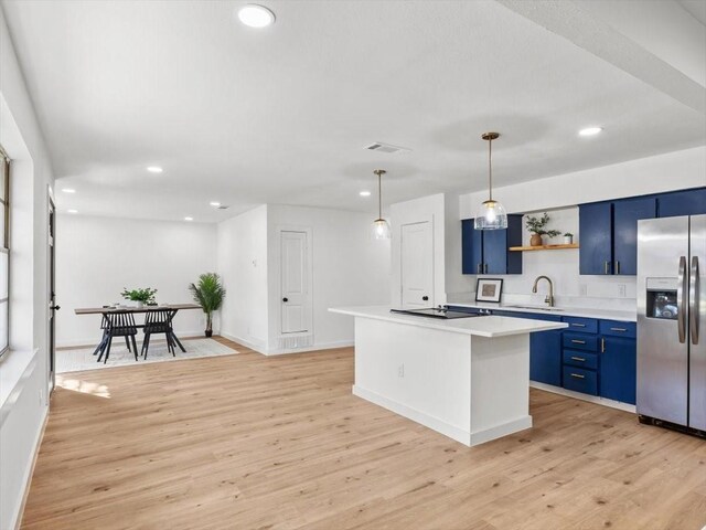 kitchen featuring blue cabinetry, hanging light fixtures, stainless steel fridge, and sink