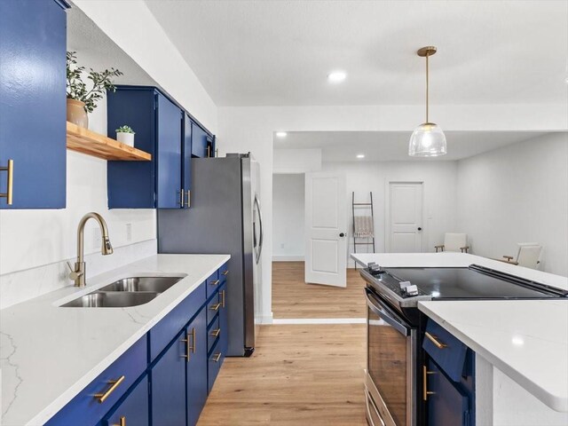 kitchen with pendant lighting, appliances with stainless steel finishes, blue cabinetry, sink, and light hardwood / wood-style flooring