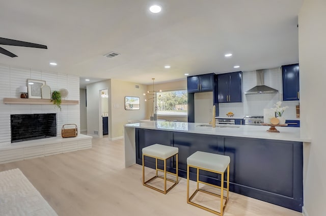 kitchen with a kitchen bar, kitchen peninsula, blue cabinets, sink, and wall chimney range hood