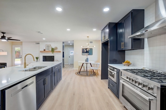 kitchen featuring decorative backsplash, appliances with stainless steel finishes, light wood-type flooring, sink, and wall chimney range hood