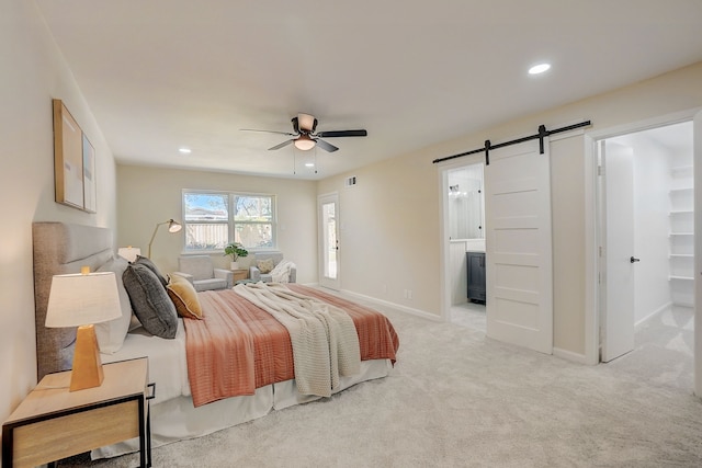 carpeted bedroom with ensuite bathroom, a barn door, and ceiling fan