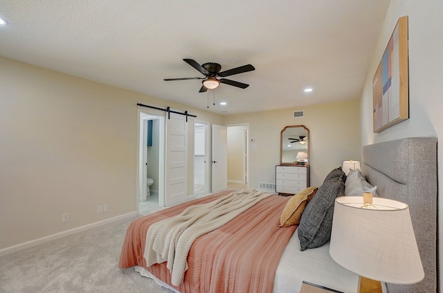 carpeted bedroom featuring a barn door, ceiling fan, and ensuite bath