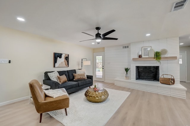 living room with wood-type flooring, a brick fireplace, and ceiling fan