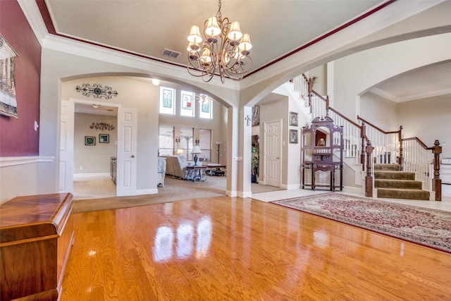 foyer featuring a notable chandelier, a towering ceiling, crown molding, and light hardwood / wood-style flooring