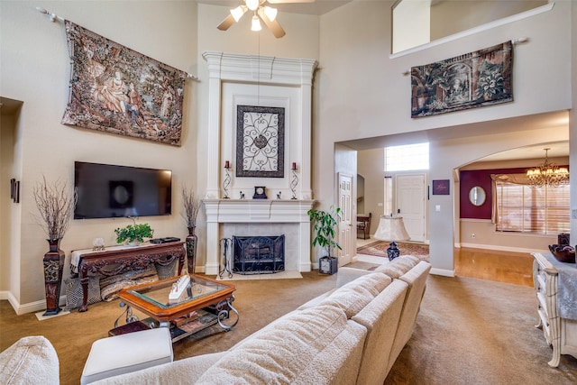 carpeted living room with a tile fireplace, a towering ceiling, and ceiling fan with notable chandelier