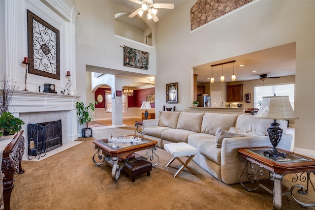 carpeted living room featuring a fireplace, a towering ceiling, and ceiling fan with notable chandelier