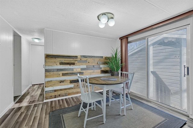 dining room with wood walls, wood-type flooring, and a textured ceiling