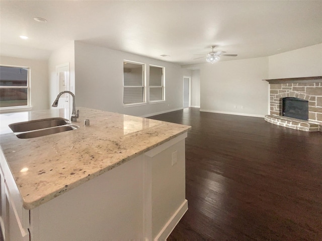 kitchen featuring sink, ceiling fan, dark hardwood / wood-style floors, an island with sink, and light stone counters