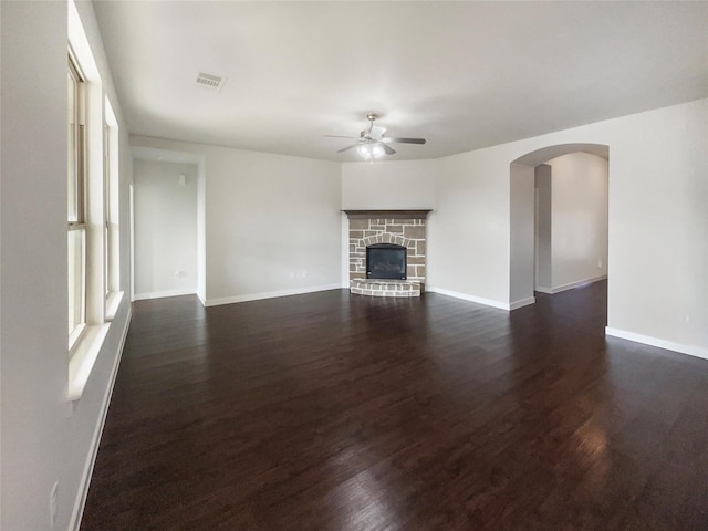 unfurnished living room with dark hardwood / wood-style floors, a stone fireplace, and ceiling fan