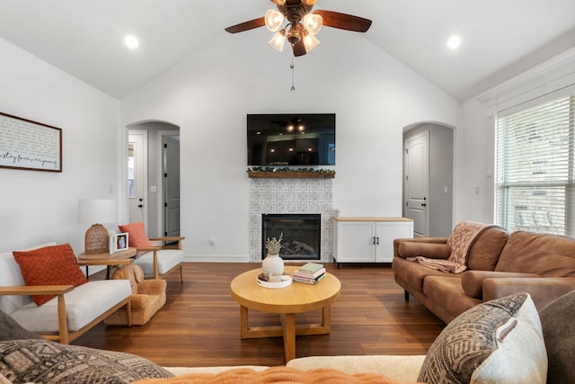 living room featuring vaulted ceiling, ceiling fan, dark wood-type flooring, and a tiled fireplace