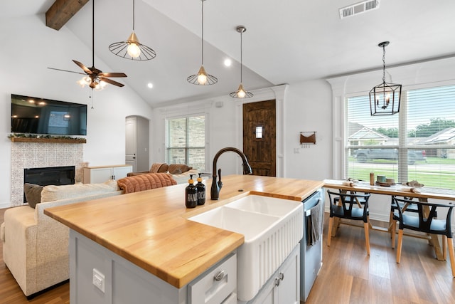 kitchen with wood counters, a fireplace, a kitchen island with sink, sink, and white cabinets