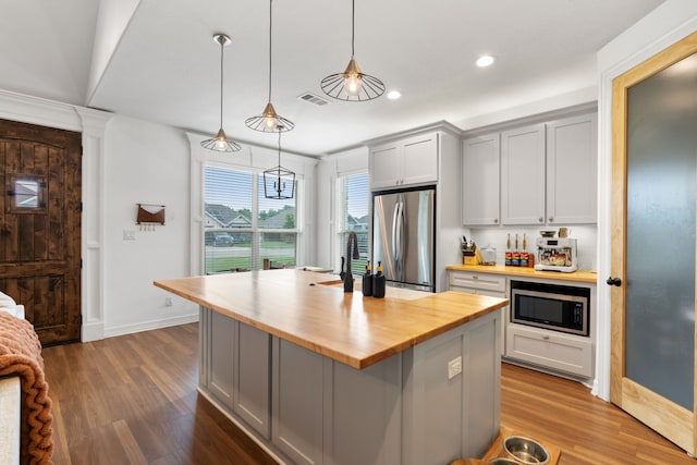 kitchen featuring butcher block counters, hanging light fixtures, gray cabinets, a kitchen island, and appliances with stainless steel finishes