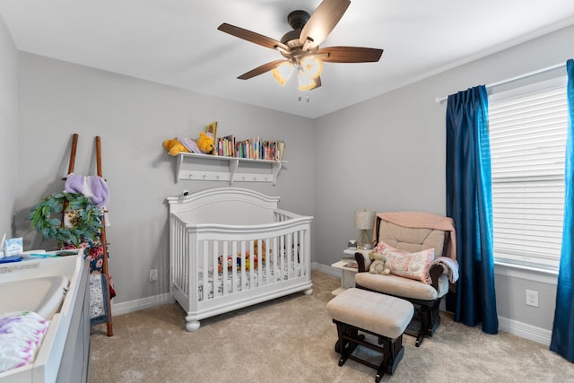 bedroom with multiple windows, ceiling fan, light colored carpet, and a nursery area