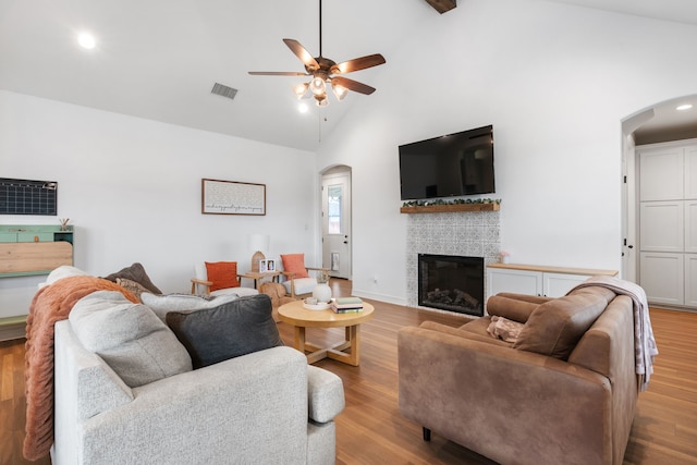 living room featuring high vaulted ceiling, ceiling fan, light hardwood / wood-style floors, and a tile fireplace