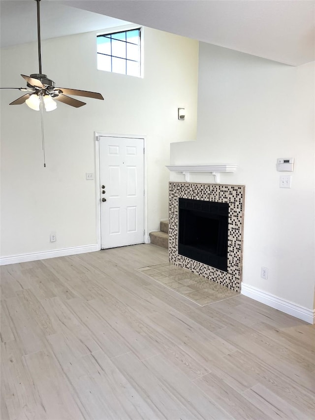 unfurnished living room featuring a tiled fireplace, ceiling fan, high vaulted ceiling, and light hardwood / wood-style floors