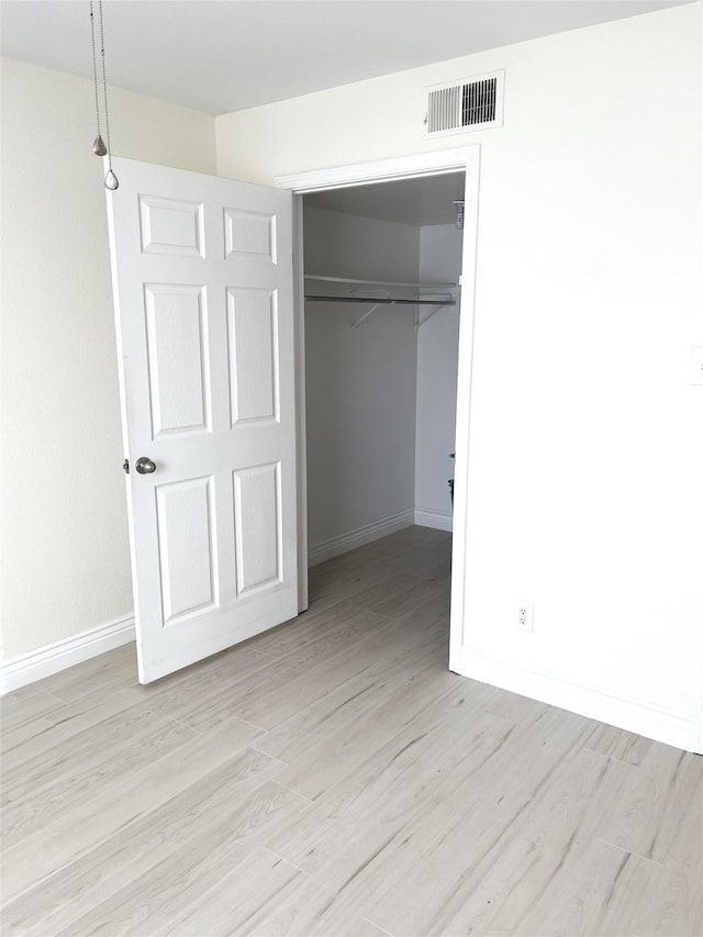 unfurnished bedroom with a spacious closet, a closet, and light wood-type flooring