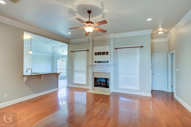 unfurnished living room featuring ceiling fan with notable chandelier, a fireplace, light wood-type flooring, and crown molding