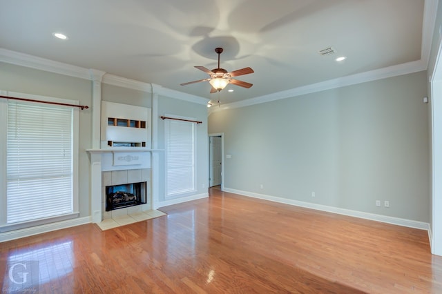 unfurnished living room with a tiled fireplace, ornamental molding, and light hardwood / wood-style floors