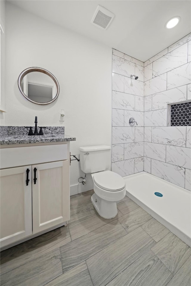 bathroom with a tile shower, vanity, and toilet