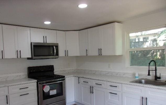 kitchen featuring white cabinets, stainless steel appliances, light stone counters, and sink