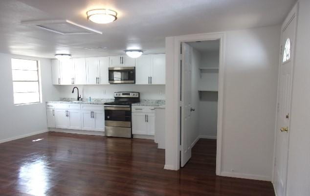 kitchen with light stone countertops, appliances with stainless steel finishes, dark hardwood / wood-style flooring, sink, and white cabinetry