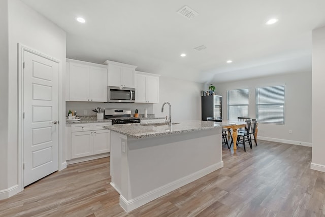 kitchen with sink, white cabinets, stainless steel appliances, and an island with sink