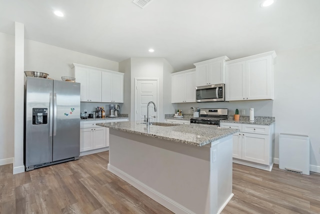 kitchen with white cabinetry, a center island with sink, stainless steel appliances, light stone countertops, and sink