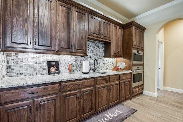 kitchen with sink, light stone counters, light hardwood / wood-style floors, decorative backsplash, and stainless steel appliances